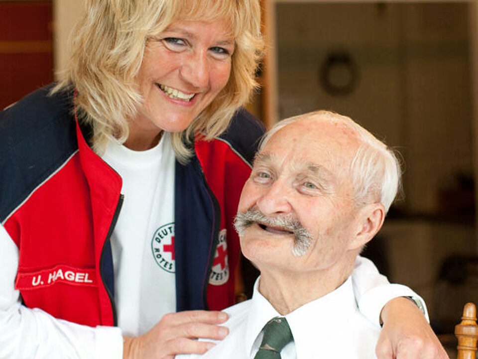 Ein lachender Senior mit einer DRK Mitarbeiterin. 